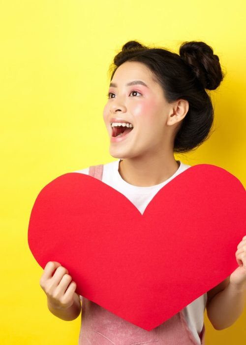 Happy valentines and love concept. Cheerful japanese girl looking left, showing big red heart and